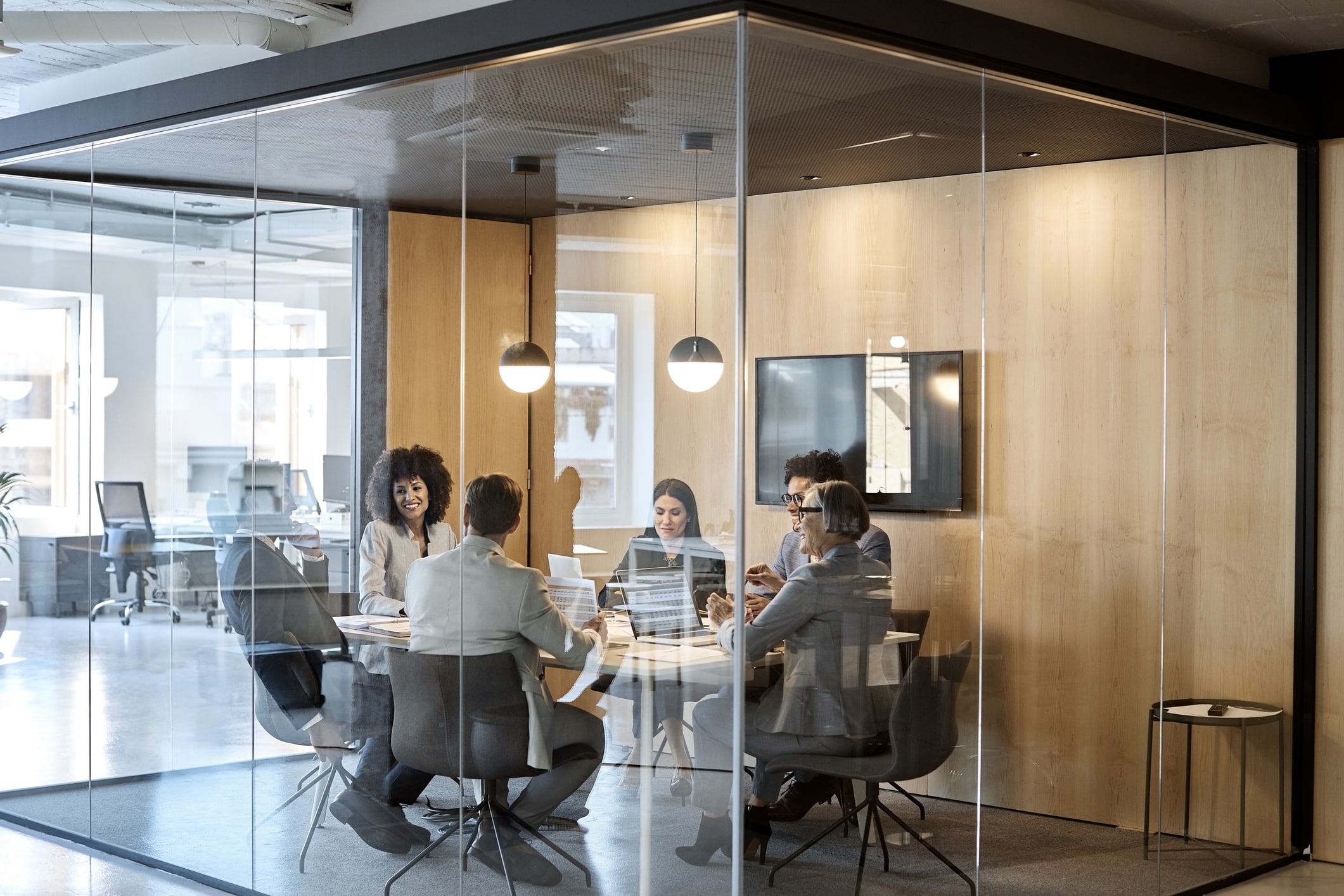 Business colleagues sitting at desk seen through glass. Multi-ethnic coworkers are discussing in board room at office. They are planning strategy.