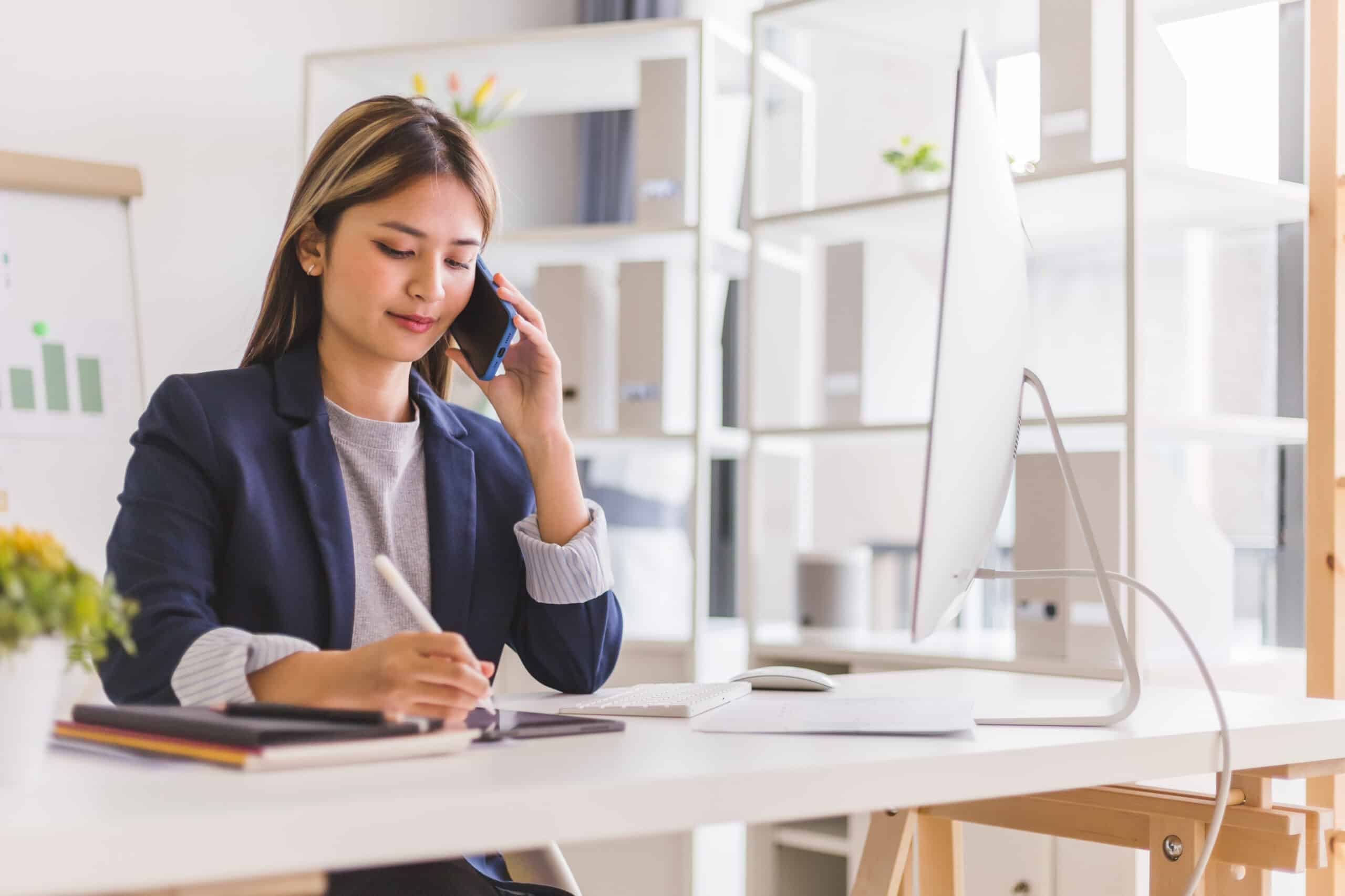 Businesswoman call phone and take a note on a tablet while sitting at the office.