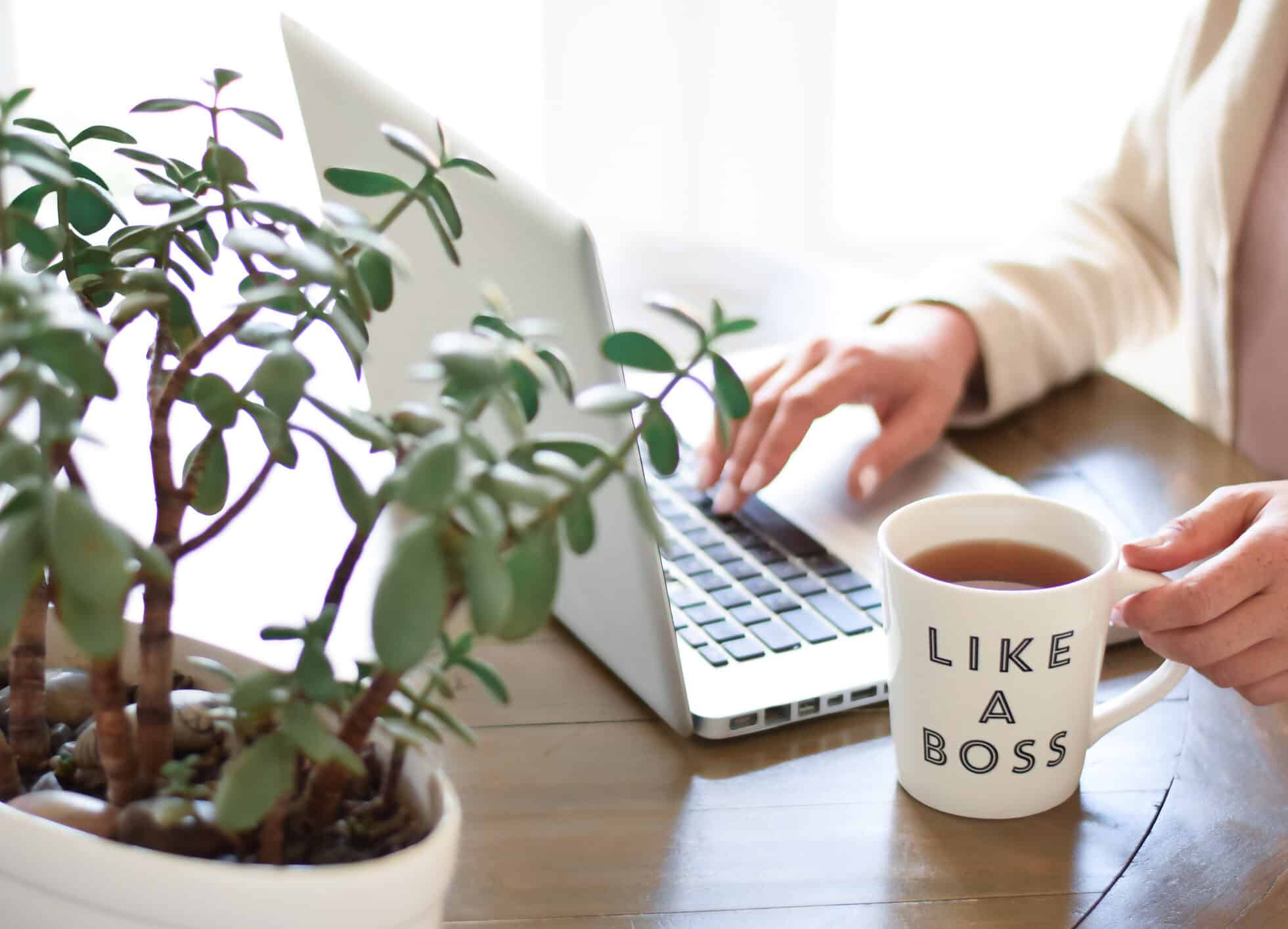 Business woman sitting at a desk typing keyboard on laptop computer with a cup of coffee on desk says Like a Boss